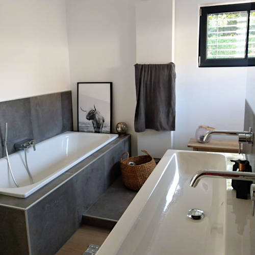 Helles Bad mit grau gefliester Wannenverkleidung und breitem Aufsatzwaschbecken