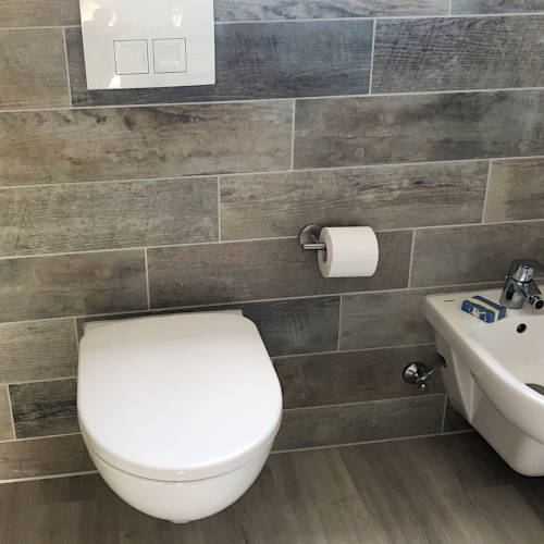 WC und Bidet vor Wandfliesen in grauer Holzoptik