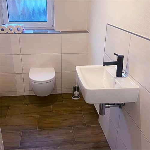 Gäste-WC mit Wand-WC und kleinem Waschbecken, weiße Wandfliesen und Bodenfliesen in Holzoptik
