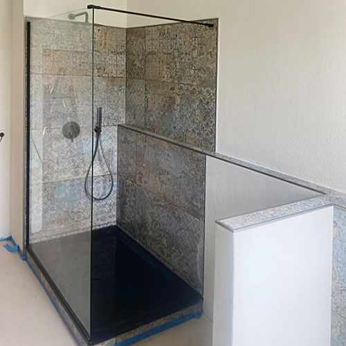 Bodengleiche Dusche mit Glaswand, schwarzer Duschtasse und gemusterten Wandfliesen