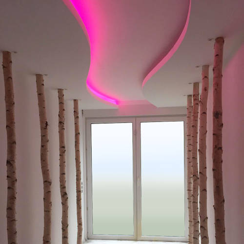 Raum mit Birkenstämmen und geschwungener Deckenkonstruktion mit pinkfarbener LED-Beleuchtung